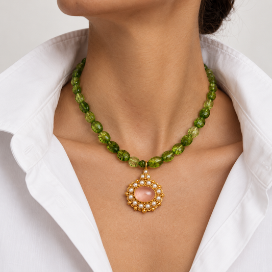 A close-up of a model wearing a green faceted bead necklace with a gold and pearl pendant featuring a pink stone from Bote A Mano, styled with a white collared shirt.