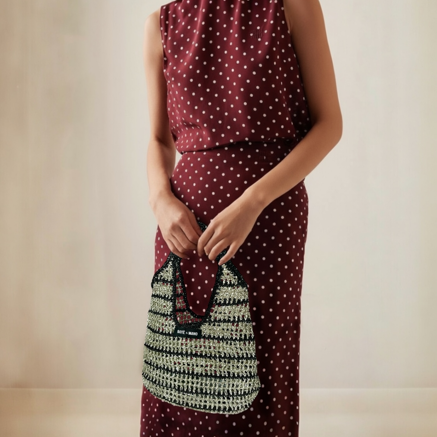 Woman wearing a burgundy dress with white polka dots holding a black and silver stripe handbag.