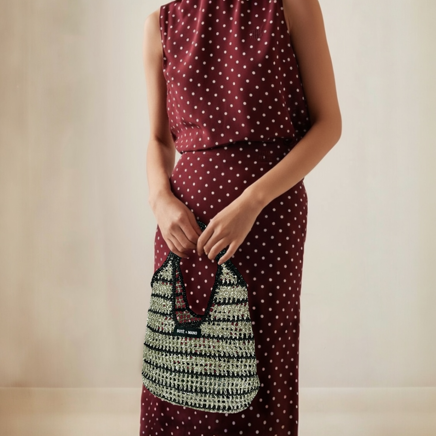 Woman wearing a burgundy dress with white polka dots holding a black and silver stripe handbag.