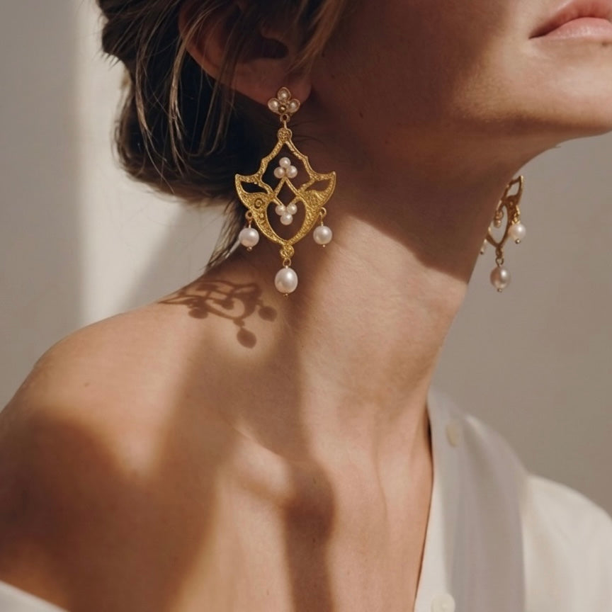 Close-up of a person wearing gold earrings with pearls against a neutral background