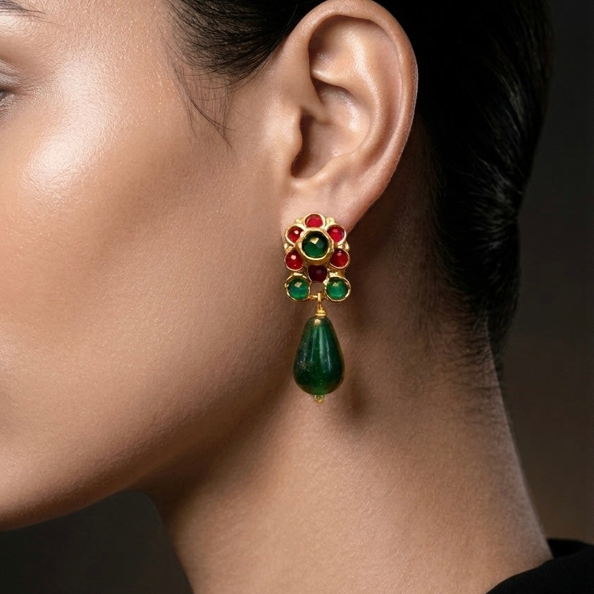 Close-up of a person wearing a green teardrop earring with gemstone details.