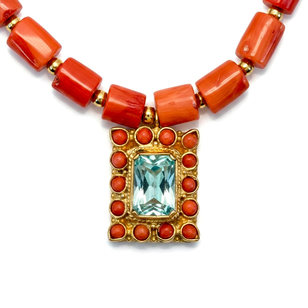 Close-up of coral and aquamarine necklace showing pendant detail with red coral and blue gemstone in gold-plated design.
